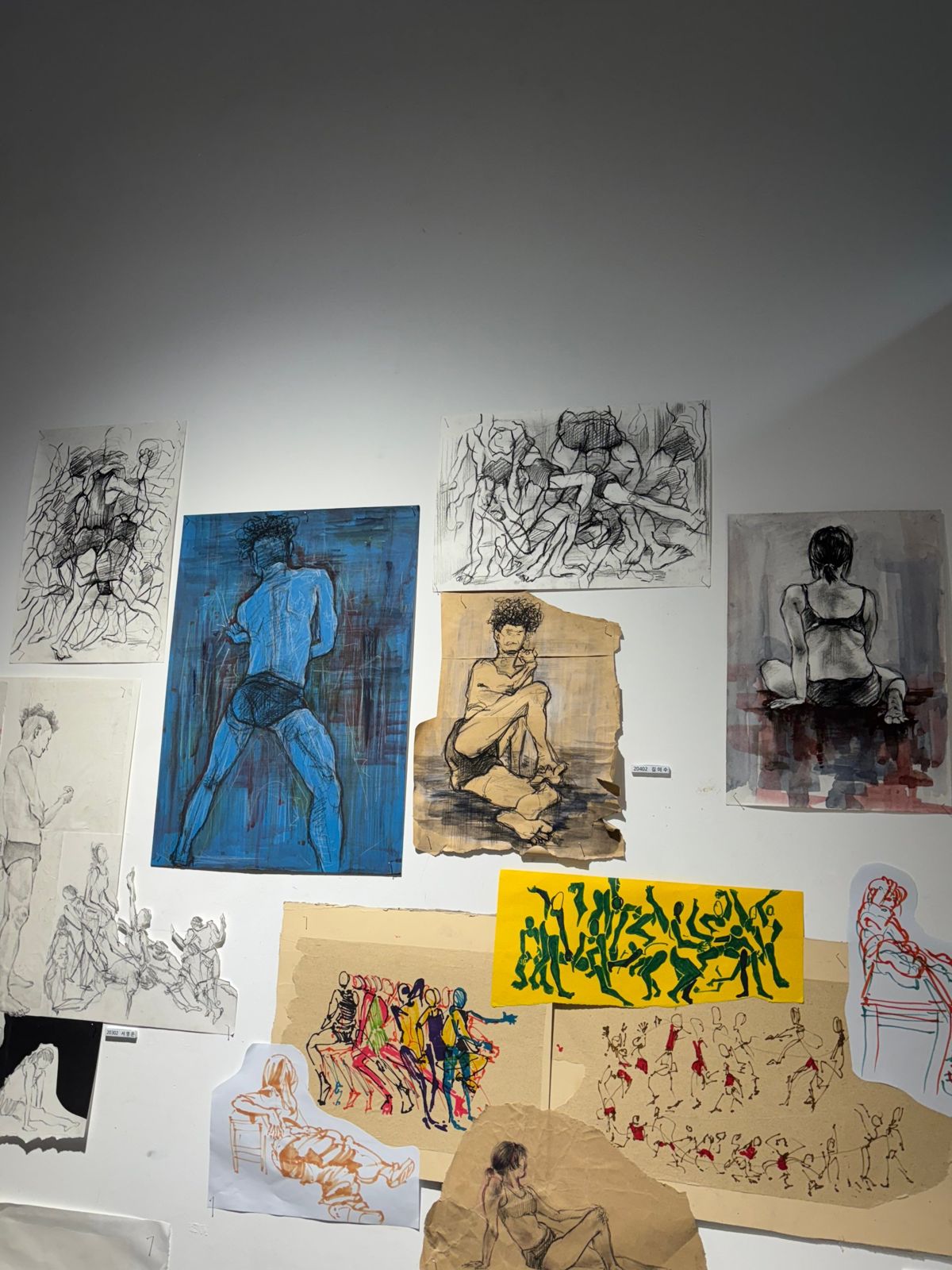 Wall of figure drawings including a blue painted figure and a seated figure on kraft paper