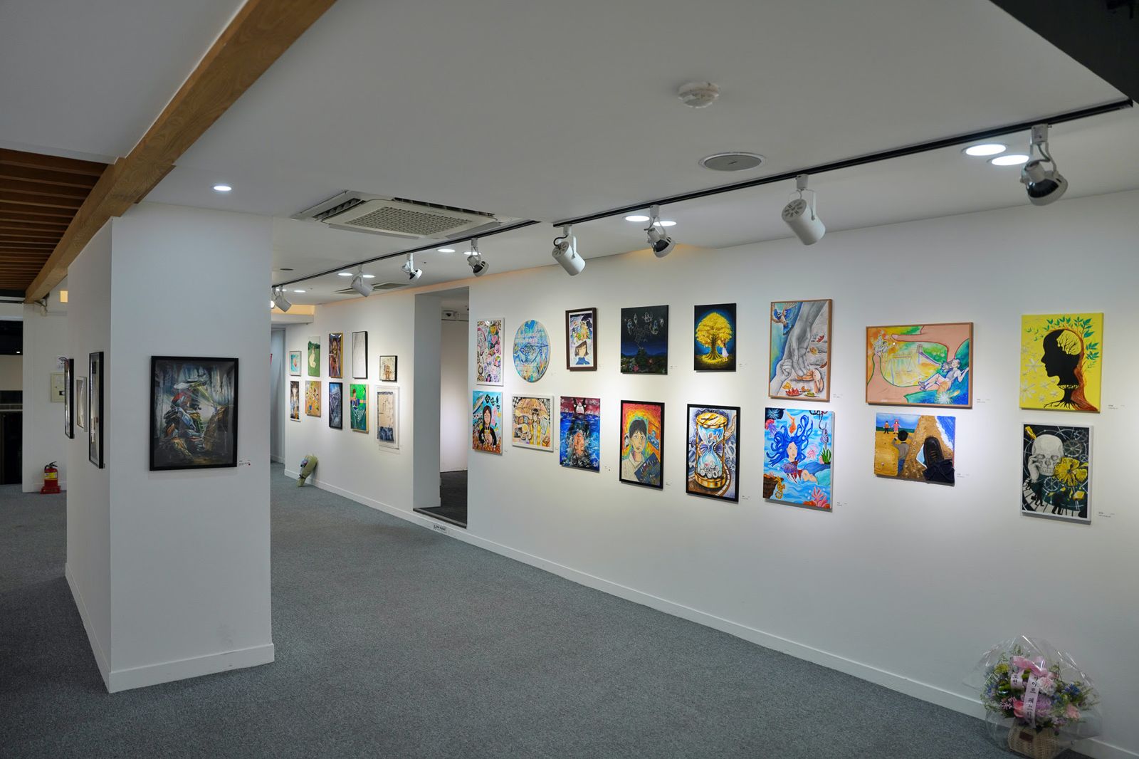 Gallery wall of student paintings under track lighting
