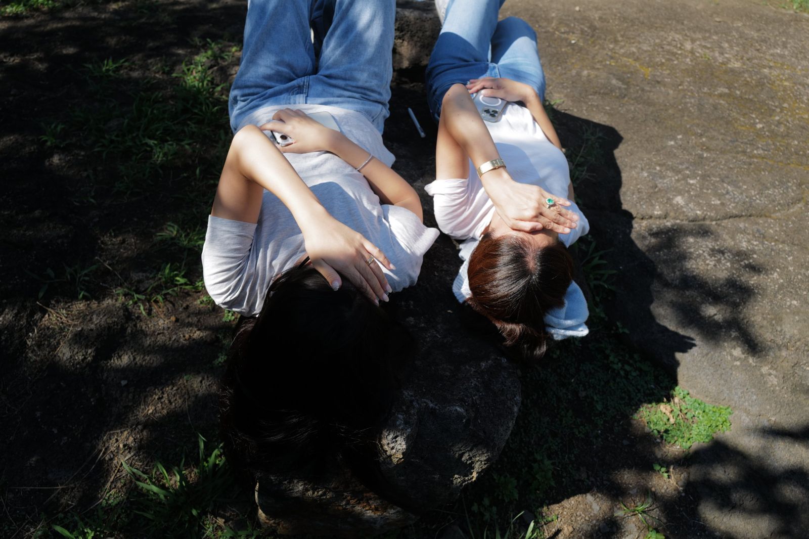 Two people in white tees and jeans lying on a sunlit rock, shading their eyes