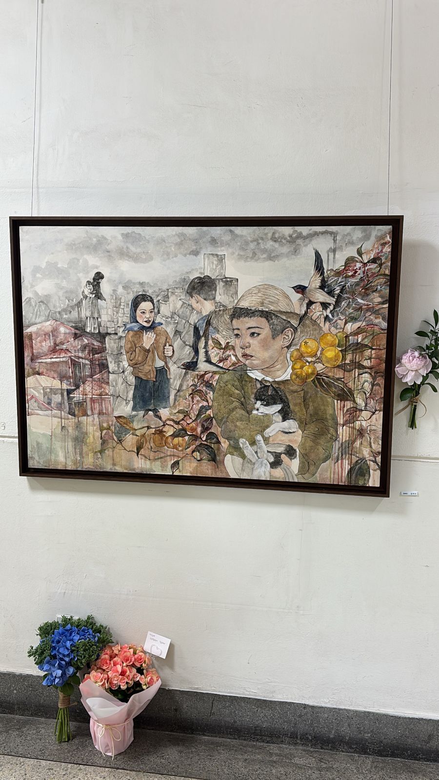 Framed painting of children, a swallow, a cat and yellow fruit against a grey industrial town